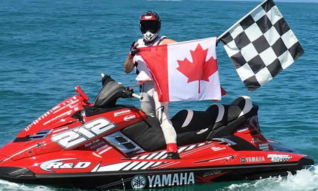 Mike Klippenstein on a PWC holding a Canadian flag and the finish line flag. 