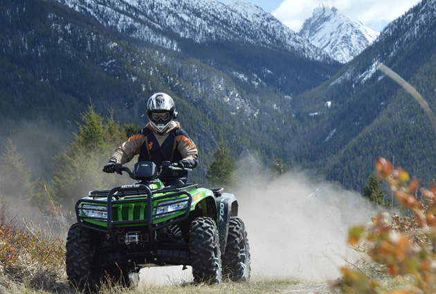A man on a green ATV with the mountains in the background. 
