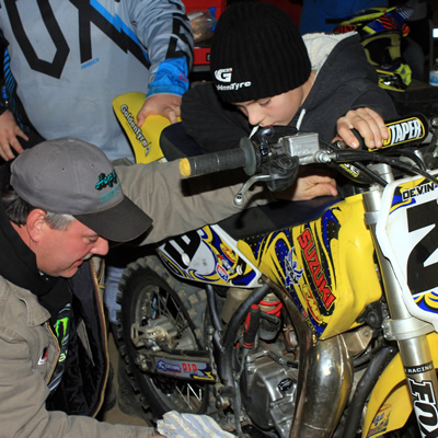A motocross father fixing his son's dirt bike. 