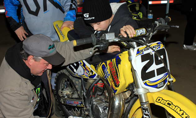 A motocross father fixing his son's dirt bike. 