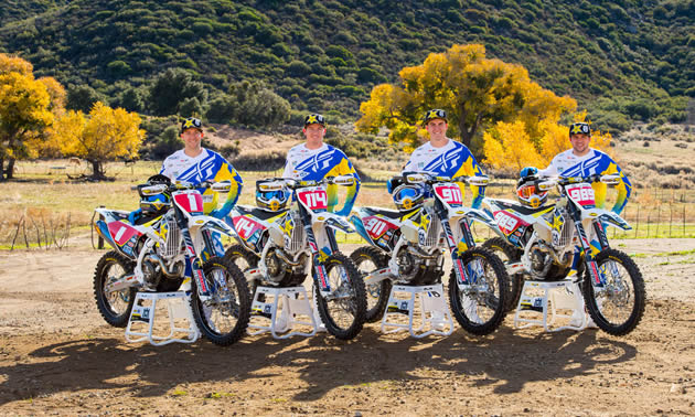 Four dirt bike riders lined up beside their bikes. 