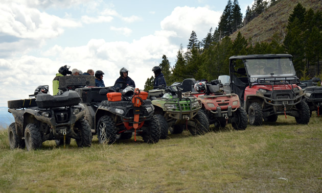 A group of ATVs or quads and a side by side parked in a row on a hilltop. 