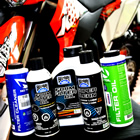Products for oiling and cleaning air filters lined up with a bike in the background. 