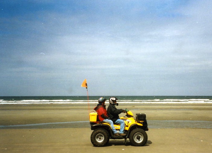 Two riders on a quad crossing an endless beach.