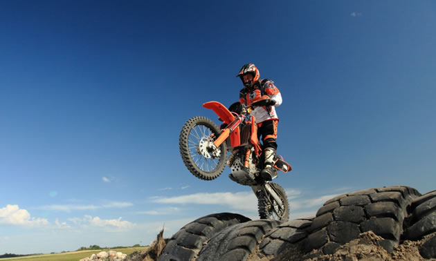 A rider on an orange KTM tackling a tire section on an endurocross track. 
