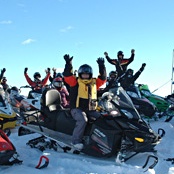26 women sitting on their parked snowmobiles with their hands in the air 