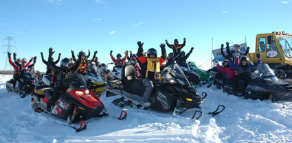 26 women sitting on their parked snowmobiles with their hands in the air 