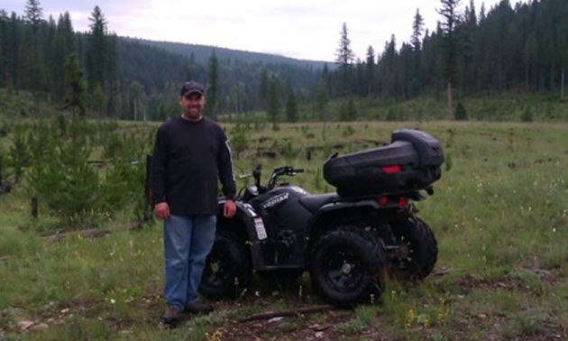 a man standing beside a quad in the backcountry