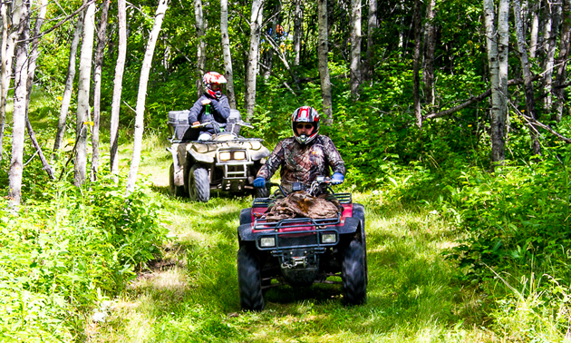 Two ATVer riding down grassy trail in Saskatchewan. 