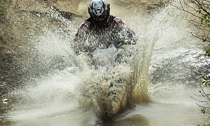 Person riding a dirt bike through water and mud