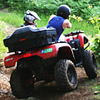 Dirt bikers watch as a person on a red ATV drives through ruts on a dirt trail. 