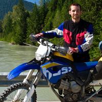 A dark haired man standing on a bridge with a dual sport bike.