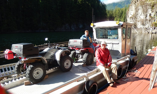 An older couple sitting on a barge with their ATVs on Powell Lake, B.C. 