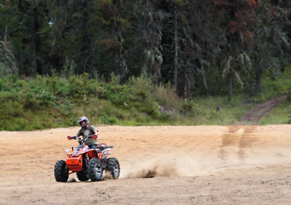 An ATVer riding through sand with forest in the background