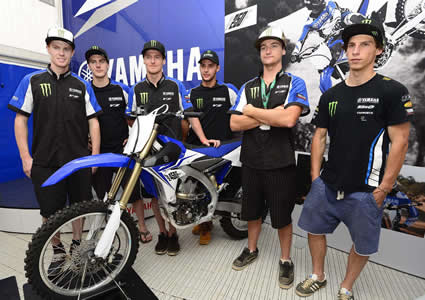 Six young men standing around a new blue dirt bike on the podium. 